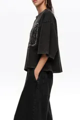 Remera corta de corte oversize color negro, confeccionada en mezcla de algodón. Presenta cuello redondo, mangas cortas amplias y un gran bordado frontal con diseño estilo etiqueta y texto.