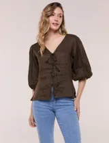 Blusa color beige confeccionada en lino, con escote en V pronunciado y cierre frontal de múltiples lazos para atar. Presenta mangas abullonadas tres cuartos con puños elásticos y corte relajado.