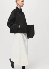 Chaqueta corta de estilo oversize en color negro, con cuello camisero, cierre frontal de botones y mangas largas con trabillas ajustables. Cuenta con dos bolsillos laterales y forro interior.