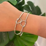 Pulsera rígida plateada con dos nudos decorativos.