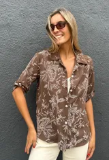 Camisa de corte recto y manga corta con cuello clásico y cierre frontal de botones. Presenta un estampado floral en color blanco sobre una base de color chocolate.