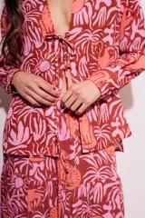 Blusa de poliéster con estampado de flores y animales en tonos rosa y marrón. Tiene cuello camisero, mangas largas y cierre frontal con lazo.