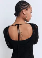 Vestido corto de crochet color negro, con cuello redondo, manga larga acampanada, espalda abierta con cierre de lazo y forro interior.