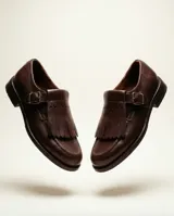 Mocasín de cuero natural color marrón chocolate, con costuras visibles, hebilla lateral metálica y solapa con flecos desmontable.