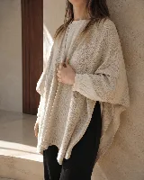 Ruana de algodón color beige, de textura suave y caída envolvente, con detalle de bordado en la espalda y aplique de cuero en el cuello.