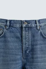 Pantalón de jean con corte recto desde la cadera y leve ensanchamiento en el bajo. Presenta tiro medio, cinco bolsillos, cierre frontal con cremallera y botón, y un acabado con efecto lavado.
