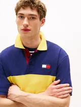 Chomba Tommy Hilfiger de corte amplio, con diseño color block en azul y amarillo, cuello clásico, cartera de tres botones, logo bordado en el pecho y logo oversize en la espalda.