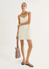 Vestido corto de corte recto y color beige, con escote en V y breteles finos con detalle de argollas metálicas.