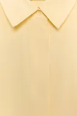 Camisa de corte fluido con cuello solapa y manga corta con dobladillo. Presenta cierre frontal con botones ocultos bajo una tapeta.