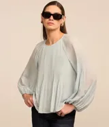 Blusa de crepé en color verde agua claro, con cuello redondo y mangas largas voluminosas. Presenta un diseño con textura plisada tanto en las mangas como en el cuerpo de la prenda, con puños ajustados.