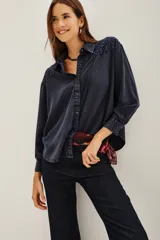 Camisa de corte amplio y holgado, confeccionada en viscosa con efecto lavado. Presenta detalles bordados en los hombros, cuello clásico, cierre frontal con botones y mangas largas con puños.