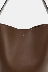 Bolso tipo saca con diseño estructurado, confeccionado en una combinación de cuero liso y gamuza en tono marrón. Cuenta con asa de hombro fija, cierre imantado y detalles metálicos en dorado.