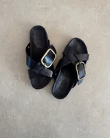 Sandalias negras de cuero con dos tiras anchas cruzadas y hebilla metálica dorada.