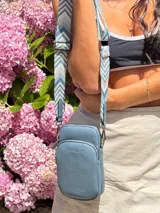 Bandolera compacta color rojo con textura de cuero, correa regulable y desmontable con diseño de rayas rojas y blancas. Cuenta con bolsillos frontales y cierre, interior forrado en tela.