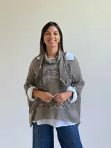 Sweater de punto color visón con diseño superpuesto, que incluye una bufanda integrada y detalles de encaje floral en el frente. Presenta mangas tres cuartos con puños abotonados y un corte holgado.