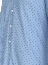 Camisa de manga larga para hombre, color celeste claro, con cuello con botones y puños abotonados. Presenta un microestampado repetitivo de cruces pequeñas en color azul oscuro.