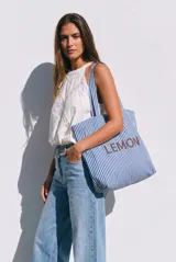 Maxi bolso tipo tote bag de algodón, con diseño de rayas verticales en color azul y blanco. Presenta asas largas para llevar al hombro y el nombre de la marca 'LEMON' impreso en el frente.
