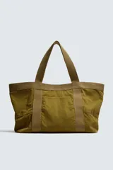 Bolso tipo shopper de gran capacidad, confeccionado en tejido con textura de pana. Cuenta con dos asas de mano resistentes, un bolsillo frontal plano y cierre principal mediante botón a presión. El interior incluye un bolsillo con cierre de cremallera.