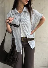 Camisa de manga corta con diseño a rayas celestes y blancas, cuello clásico y cierre frontal de botones.