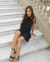 Vestido corto negro con cuello halter regulable, diseño sin mangas y falda con volados superpuestos.