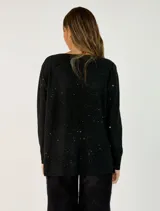 Sweater de punto color beige con sutiles destellos brillantes, cuello redondo, manga larga con puños acanalados y diseño asimétrico con el ruedo trasero más largo que el delantero.