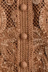Cropped top de manga larga color marrón en punto estilo crochet con diseño en hilo de chenilla y ribetes festoneados. Cuenta con escote en U y botones forrados al frente, con forro de punto.