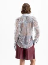 Camisa transparente de mesh rayado con bordados de dragones en verde y naranja. Tiene cuello clásico, botones negros forrados, puños de popelina y mangas abullonadas.