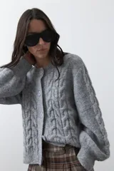 Cardigan de tejido de punto color marrón chocolate, con diseño de trenzas en el frente y mangas. Presenta cuello redondo, cierre frontal con botones al tono y puños acanalados.