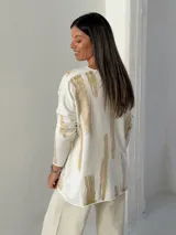 Sweater de punto con cuello en V y mangas largas, de diseño holgado. Presenta un estampado abstracto con pinceladas en color dorado sobre una base blanca.