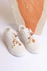 Zapatillas bajas color marrón con cordones y charms dorados.