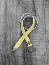 Cinto amarillo pastel con hebilla metálica labrada y puntera metálica labrada.