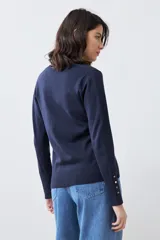 Cardigan de punto negro con escote en V, cierre frontal con botones metálicos dorados y mangas largas con puños ajustados que incluyen detalles de botones decorativos.