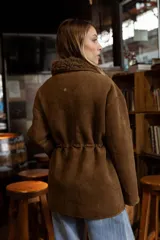 Campera de efecto gamuza color tostado con interior de corderito sintético. Presenta cierre frontal, bolsillos delanteros con solapa, cintura ajustable con cordón y puños con detalle de corderito.