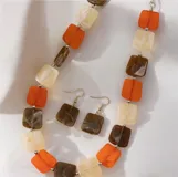 Collar de diseño geométrico compuesto por piezas rectangulares de resina en tonos naranja, marrón y crema, unidas por pequeñas cuentas metálicas plateadas.