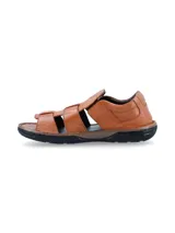 Sandalias de cuero color tostado con diseño de tiras cruzadas y cierre de velcro en el lateral, con suela de goma negra y plantilla marrón oscura.