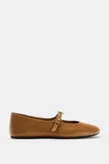 Zapato tipo bailarina de piel color marrón tostado, con tira delantera ajustable, aplique metálico y punta redonda.