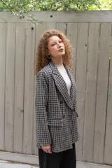 Blazer cruzado de paño con patrón a cuadros en tonos blanco y negro, de corte recto y largo medio, con solapas de muesca, bolsillos con solapa en los laterales y cierre frontal de dos botones oscuros.