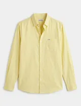 Camisa de manga larga color amarillo, confeccionada en algodón con textura tipo lino. Presenta cuello clásico, cierre frontal con botones de pasta y un bolsillo en el pecho con una pequeña etiqueta con el logo de la marca.