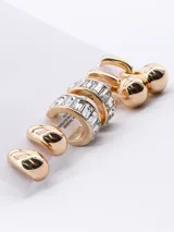 Set de tres pares de aros dorados. Un par de aros tipo argolla con forma de gota, un par de aros tipo argolla con incrustaciones de strass y un par de aros tipo argolla con dije de esfera colgante.