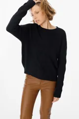 Sweater de punto negro con diseño de trenzas verticales en el frente y cuello redondo. Presenta un corte holgado con puños y ruedo acanalados.