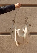 Cartera de cuero roja con tachas plateadas en el borde inferior, doble asa de cuero y cierre superior.