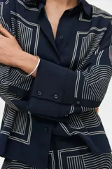 Camisa de sarga de corte oversized, color azul marino, con estampado geométrico de líneas blancas. Presenta cuello clásico, cierre frontal con botones, hombros caídos y mangas largas con puños abotonados.