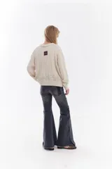 Cardigan de tejido de punto color marrón, con cuello solapa, cierre frontal de cremallera y diseño de trenzas. Cuenta con puños y dobladillo en rib elástico y un pequeño bordado en el pecho.