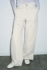 Jeans de tiro medio color blanco roto, con corte ancho y pierna recta. Presenta detalles de trabillas y pespuntes visibles, y bolsillos laterales y traseros.