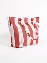 Bolso tipo tote grande, resistente al agua, con diseño de rayas verticales rojas y blancas. Cuenta con asas largas de hombro, cierre superior y parche de cuero con logo grabado. Incluye neceser transparente a juego con base y detalles a rayas.