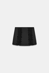 Falda pantalón negra de satén con detalles de encaje vertical y aberturas frontales. Cuenta con cierre lateral oculto.