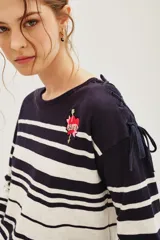 Remera de manga larga a rayas horizontales en azul marino y blanco, con cuello redondo y detalle de parche bordado en forma de corazón con flecha en el pecho. Presenta lazos decorativos en los hombros.