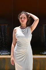 Vestido largo de fiesta color gris claro metalizado, con escote redondo, sin mangas y abertura lateral en la falda. Presenta un drapeado lateral que estiliza la figura.