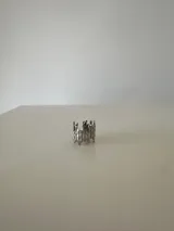 Anillo de diseño orgánico y abstracto, con forma de gotas o filamentos verticales unidos, fabricado en acero quirúrgico de color plateado.