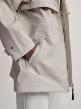 Piloto de lluvia color beige con capucha y cierre frontal.